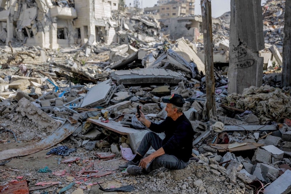 Seorang Warga Palestina Mencoba Mengakses Internet via Ponsel di Tengah Reruntuhan Bangunan di Jalur Gaza Pasca Serangan Bom Israel 24/11/2023. (AFP/Getty/IFEX)